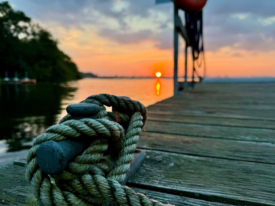 Aufgeschossenes Tau auf einem Holzsteg, dahinter geht die Sonne über dem See unter