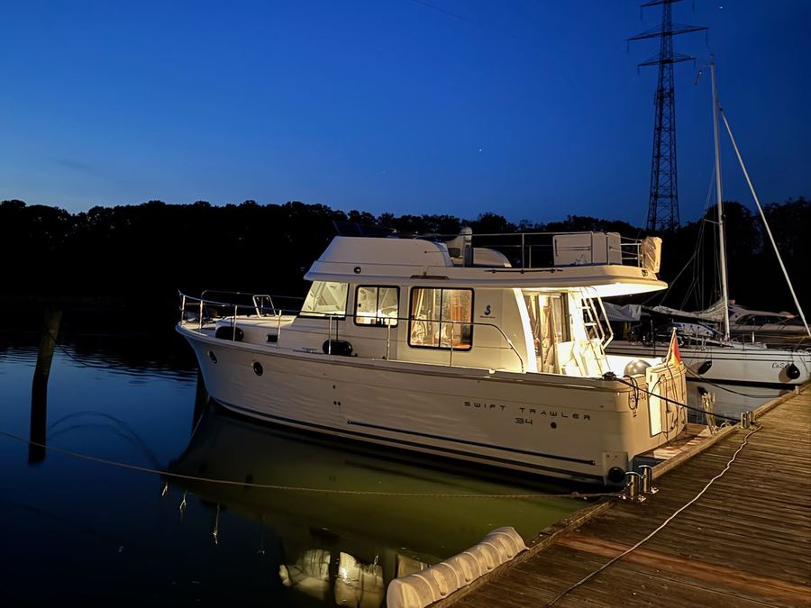 Motoryacht am Holzsteg zur blauen Stunde, das Boot spiegelt sich im ruhigen Wasser