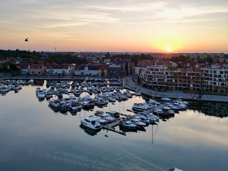 Hafenbecken mit vielen Booten im Abendlicht, ein Motorboot zieht eine Spur durchs Wasser