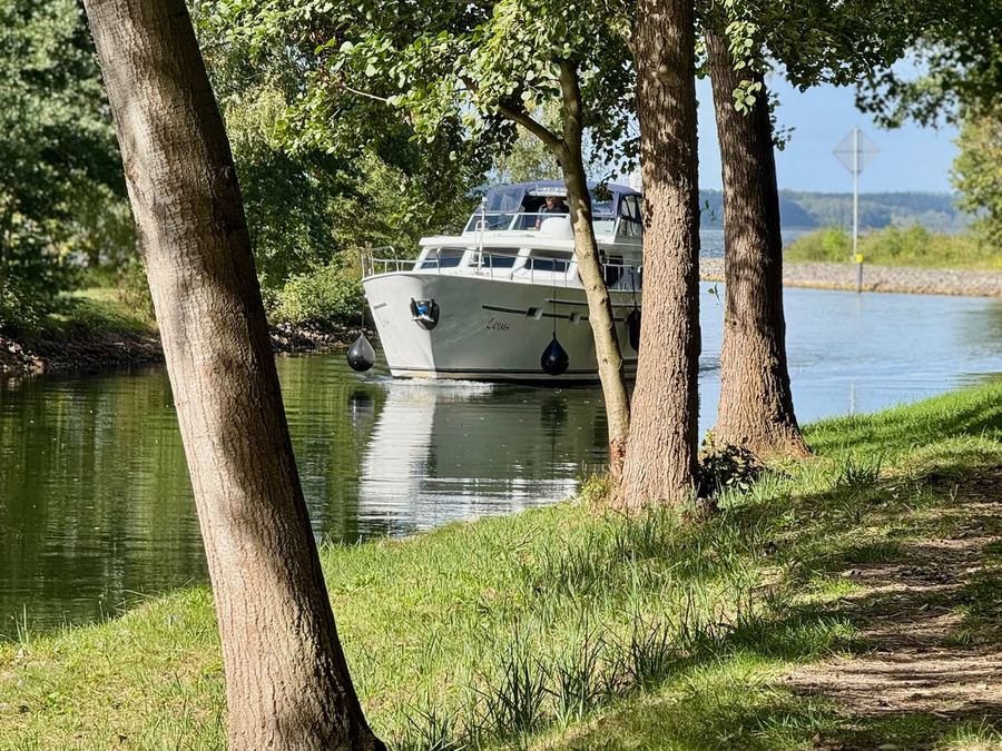 Motoryacht am Ufer, gesehen durch Bäume an einem Uferweg