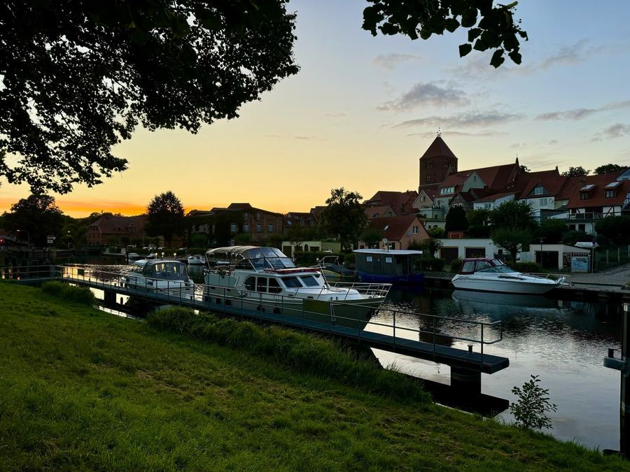 Uferort mit Backsteinkirche und Booten am Steg im Abendlicht